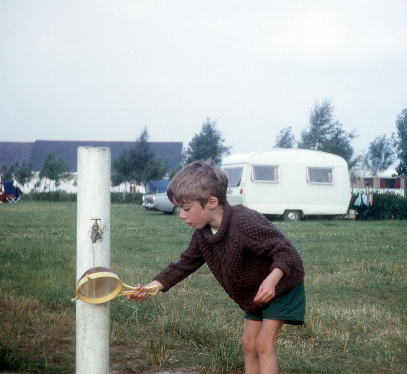 7102212k May 1971 - Jon cleaning the sieve under a tap at the Benodet campsite.